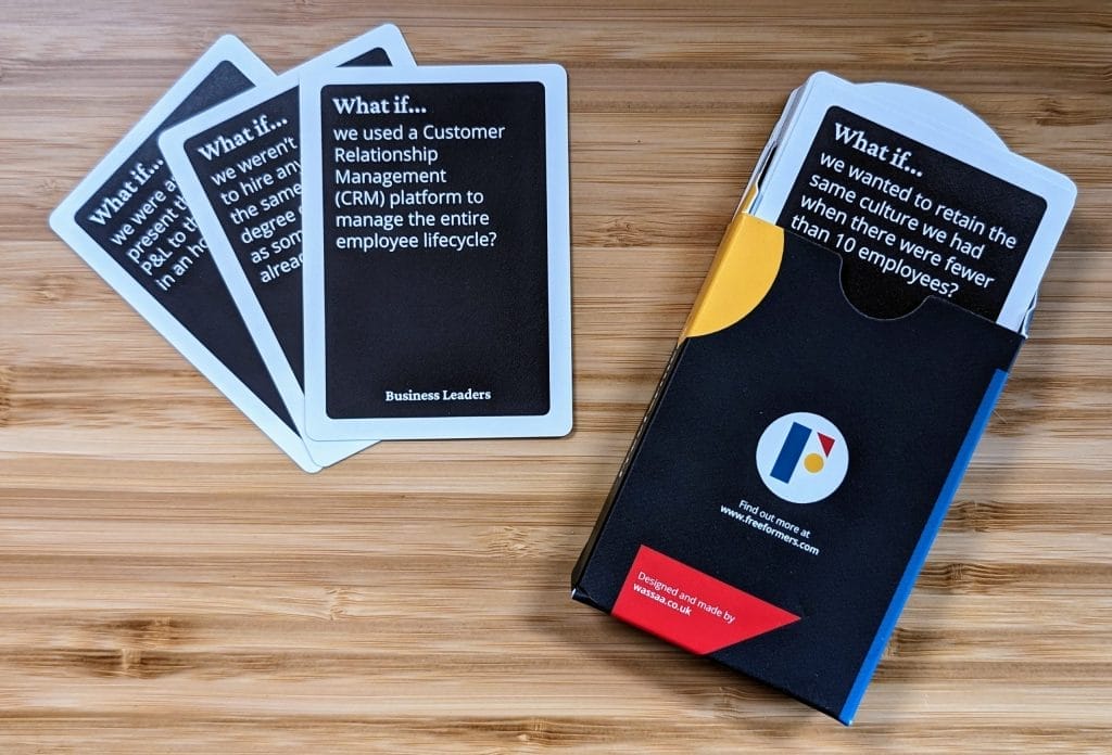 Image contains three playing cards and a box. Only the text on the first card is visible and reads "what if we used a Customer relationship Management (CRM) platform to manage the entire employee lifecycle?" There is a card poking out the box which reads "what if... we wanted to retain the same culture we had when there were fewer than 10 employees?"  The box is black with the Freeformers logo.